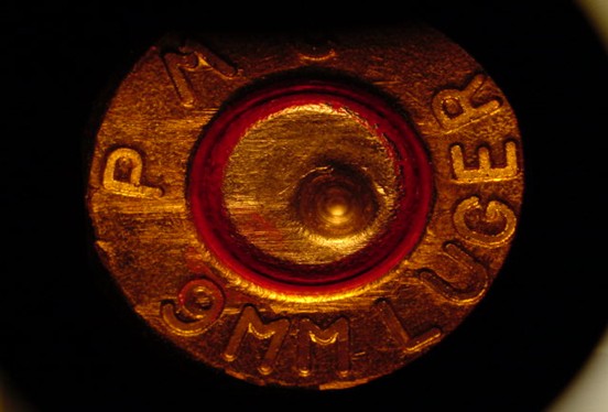 A fired 9mm Luger cartridge case with visible firing pin and breech face impressions.